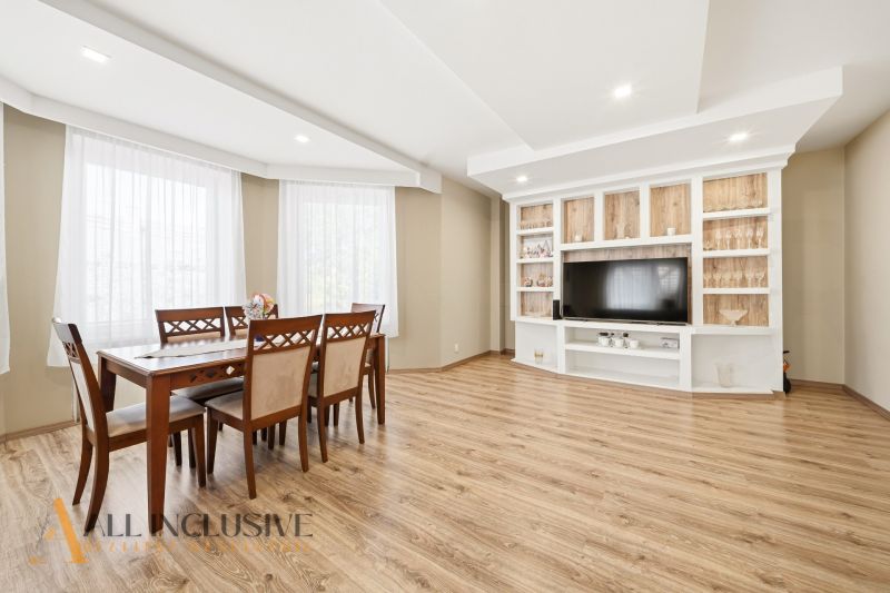 A dining room with a wood-patterned floor and a TV wall in a family house.