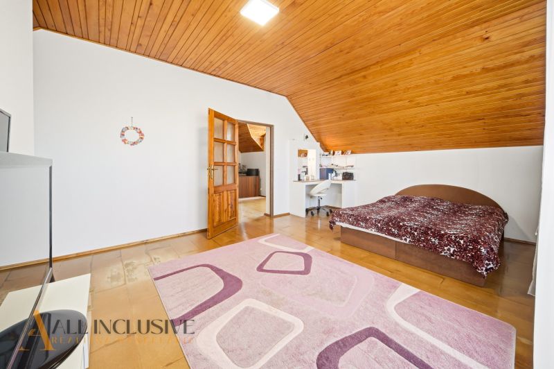 A bedroom in a family house with a wood-patterned floor, a bed, and a desk.