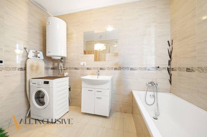 Bathroom in a 3-room apartment with a washing machine, bathtub, and beige tiles.