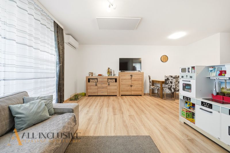 A living room in a three-room apartment with a wooden decor floor and a children's kitchen.