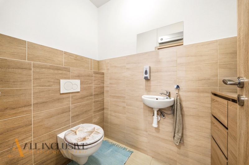 A bathroom in a 3-room apartment with wood decor tiles, a white sink, and a toilet.