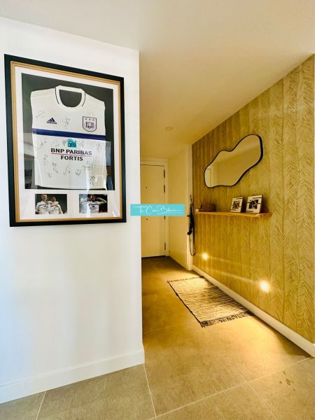 A hallway in a 3-room apartment with a mirror, lighting, and a football jersey on the wall.