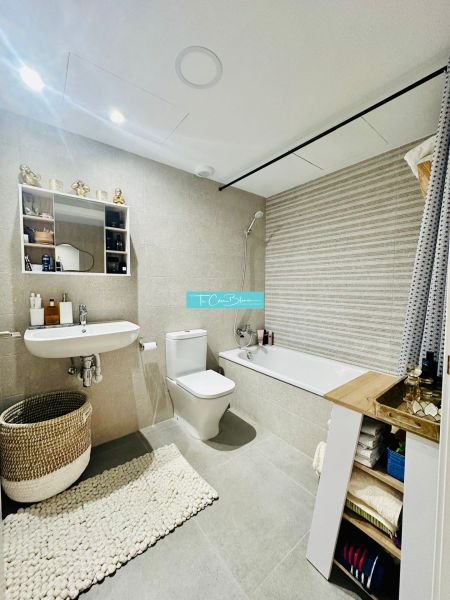 A bathroom in a 3-room apartment with a bathtub, sink, toilet, and light tiles.
