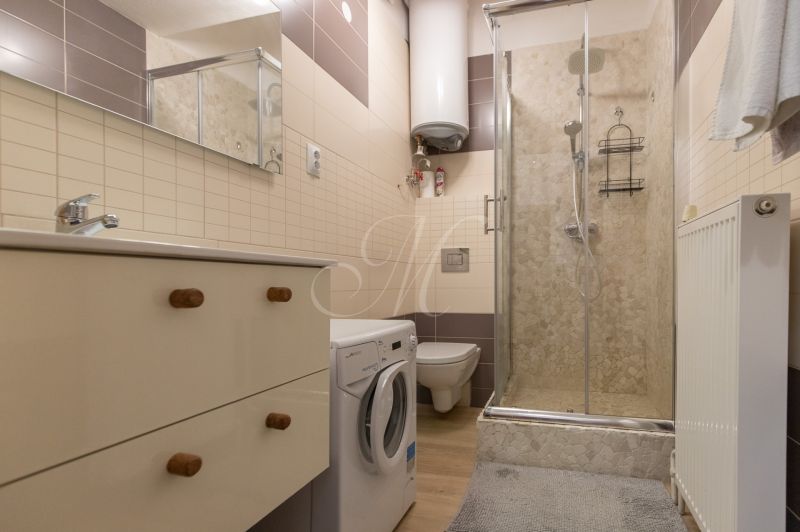 A compact bathroom in a 2-room apartment with a washing machine, shower, and sink.
