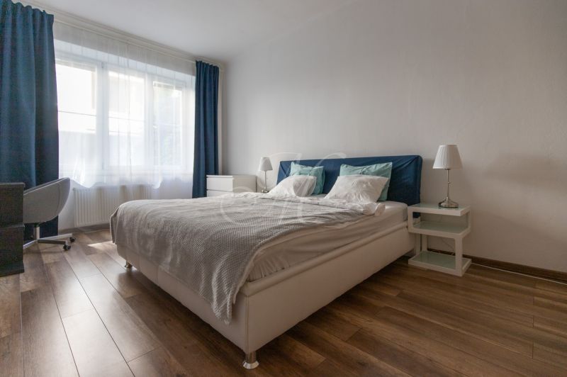 Bright bedroom with a bed and an office chair in a 2-room apartment, floor with wooden decor.