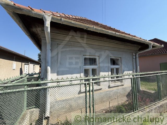A family house in Šurany with white windows and a red roof behind a fence.