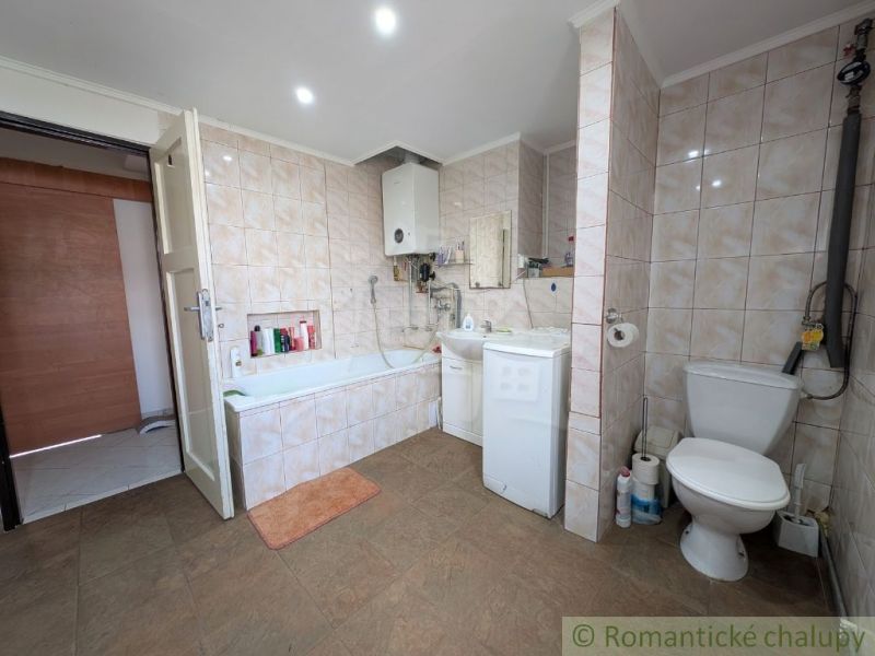 Bathroom in a 2-room apartment with a bathtub and a washing machine, tiled with light tiles.