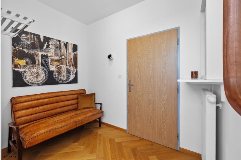 Entrance hall with a brown sofa, a painting, and a floor with a wooden decor in a 4-room apartment.