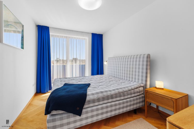 A bright bedroom with a patterned bed in a 4-room apartment with wood-patterned flooring.