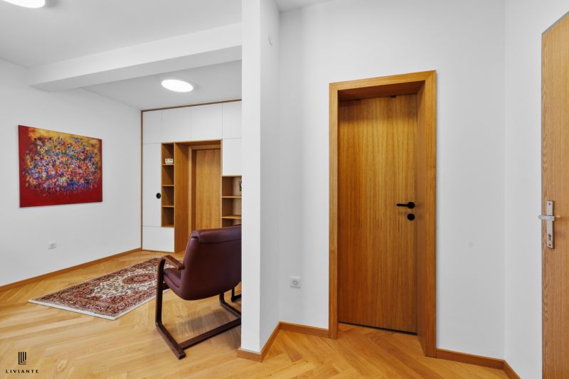 A hallway in a 4-room apartment with a wooden decor floor, a painting, and a comfortable armchair.