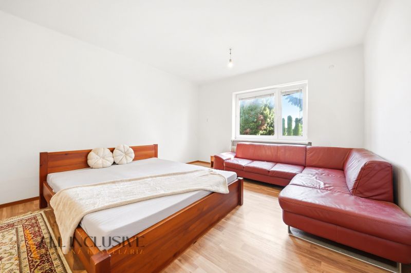 A bedroom in a family house with a wooden decor floor, a red sofa, and a bed.