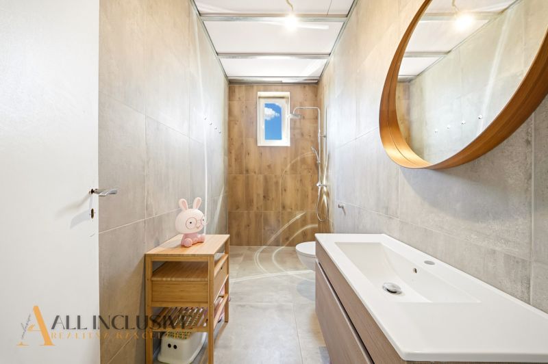 A bathroom in a family house with a wooden decor floor, a shower, and a round mirror.