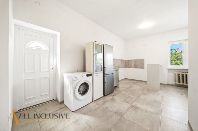A kitchen in a family house with a washing machine and a refrigerator on the tiles.