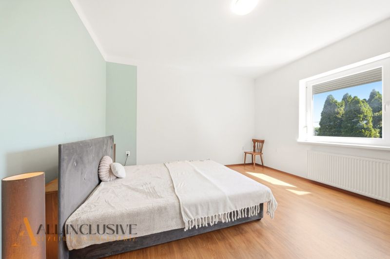A bedroom in a family house with a light wall, a bed, and a wooden decor floor.