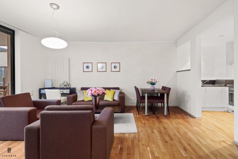 Living room with wood-patterned flooring, furniture, and a table in a two-room apartment.
