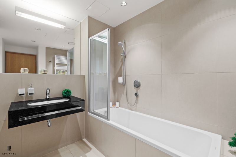 A bathroom in a 2-room apartment with a bathtub, a sink, and a large mirror.