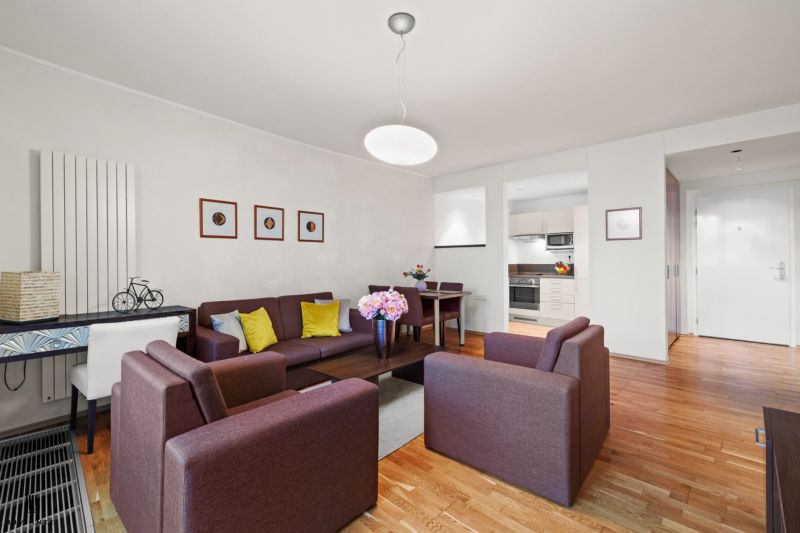 A living room with colorful sofas, wooden decor flooring, and a dining table in a two-room apartment.