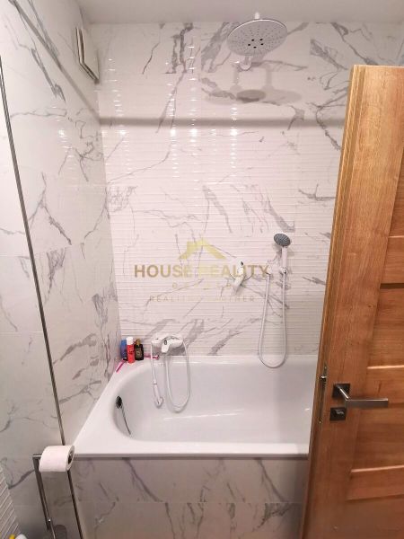 Bathroom in a 2-room apartment with a bathtub, marble tiles, shower head.