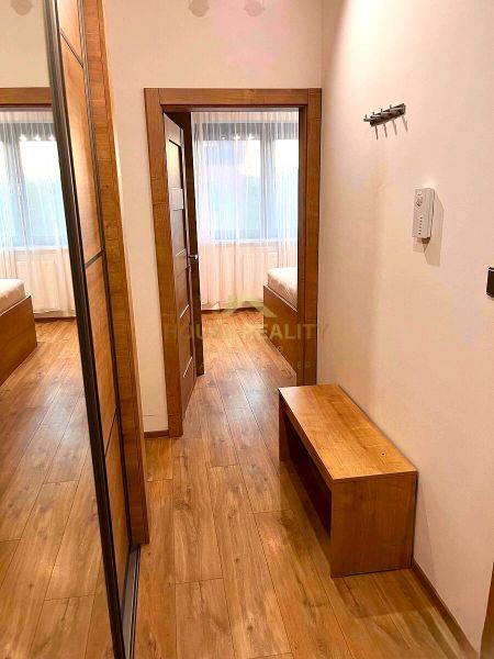 A hallway in a 2-room apartment with a wooden decor floor, a mirror, and a bench.