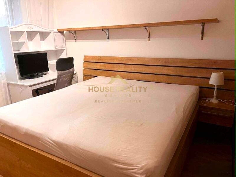 Bedroom in a 2-room apartment with a bed, table, shelf, and desk lamp.