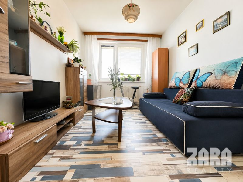 Living room with a sofa and a wooden-decor floor in a three-room apartment.