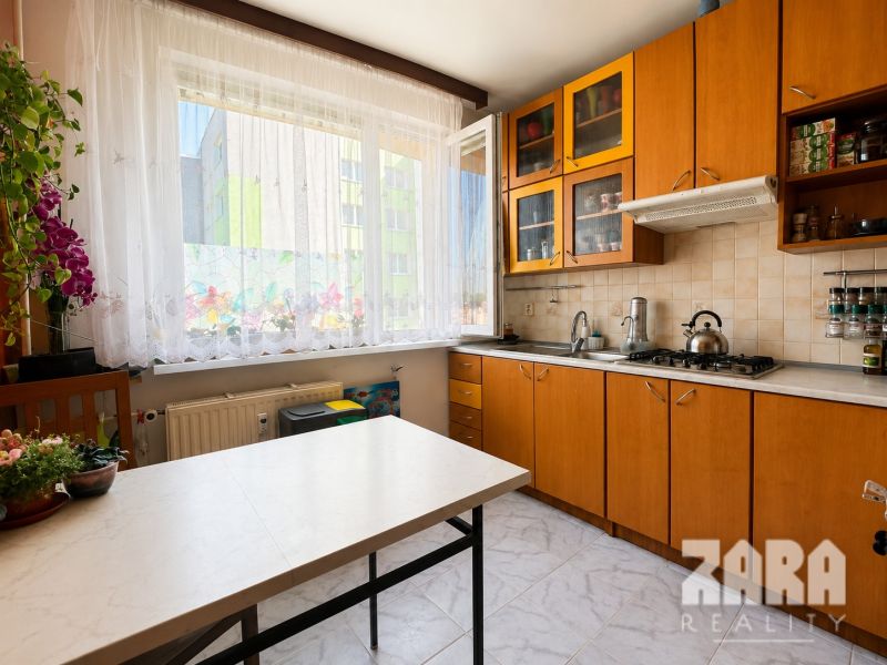A kitchen in a 3-room apartment with a view, wooden cabinets, flowers on the window.