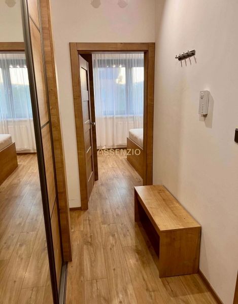 A hallway in a 2-room apartment with a wooden decor floor and a mirror on the wall.