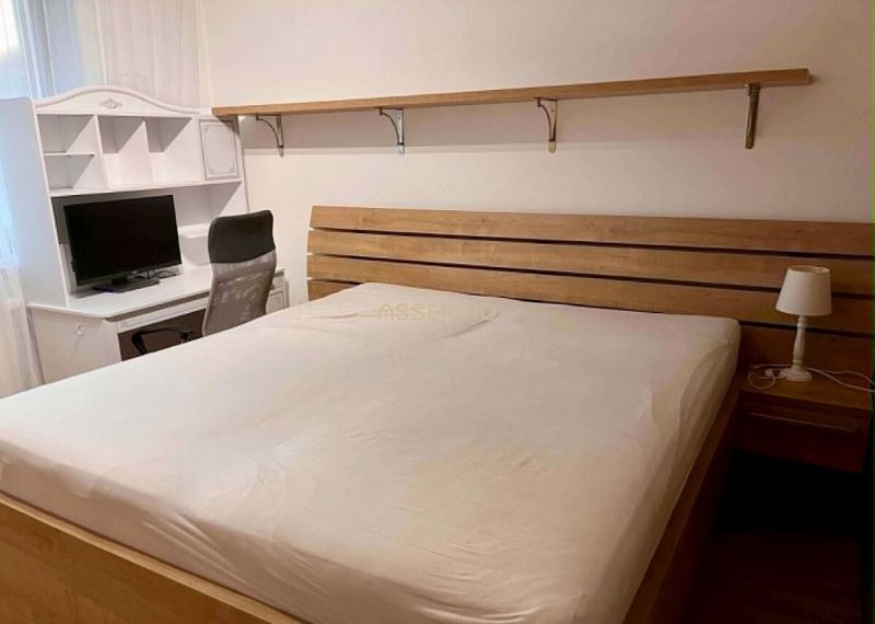 A bedroom with a wooden bed, a table, and a computer desk in a two-room apartment.