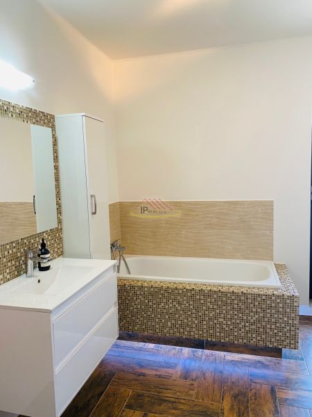 A bathroom in a family house with a bathtub, a sink, and a wooden decor floor.