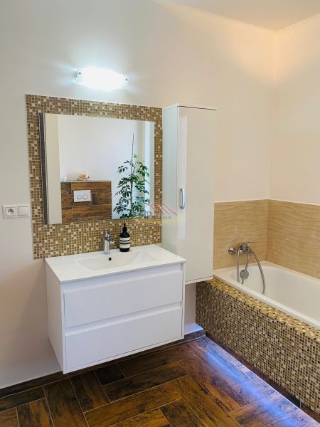 A bathroom in a family house with a mirror, a bathtub, and a floor with a wooden decor.