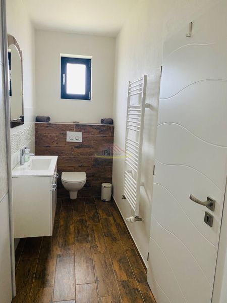 A bathroom in a family house with a wooden decor floor, a white sink, and a window.