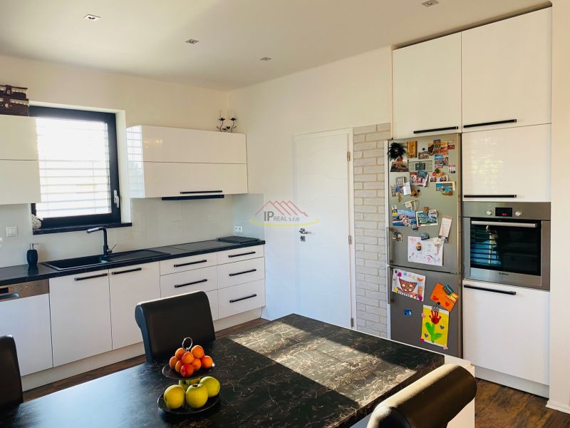 A kitchen in a family house with white cabinets, a dark table, and wooden decor flooring.
