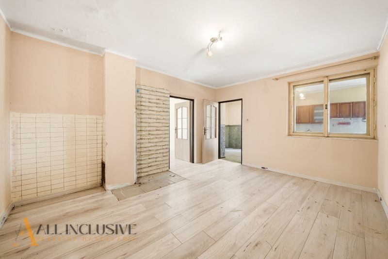 A room in a family house with a wooden decor floor and a door to the kitchen.