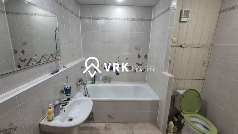 A bathroom in a 3-room apartment with a bathtub, a sink, a mirror, and a green toilet seat.