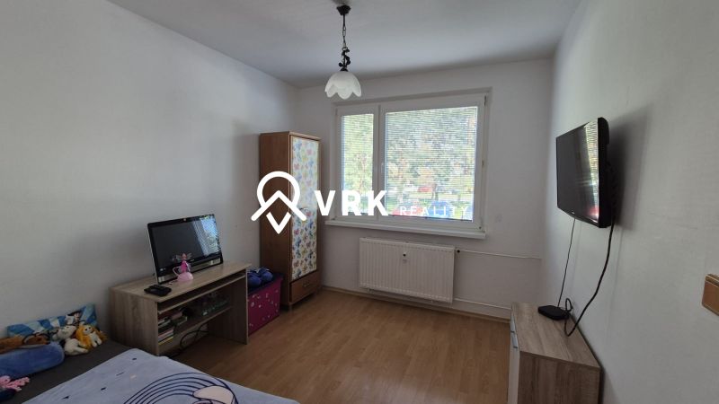 A room in a 3-room apartment with a wood-patterned floor, a television, and a window.