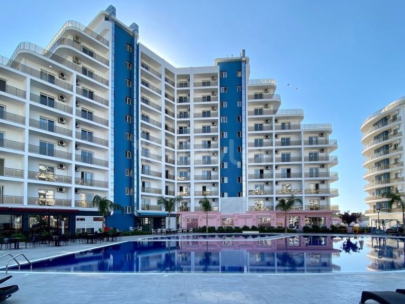 Residential complex in Iskele with a swimming pool, surrounded by tall buildings and palm trees.