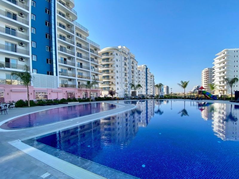 Apartment houses in Iskele with a swimming pool and palm trees in the area.