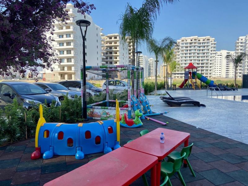 A children's playground by the pool and modern apartment buildings in the city of Iskele.