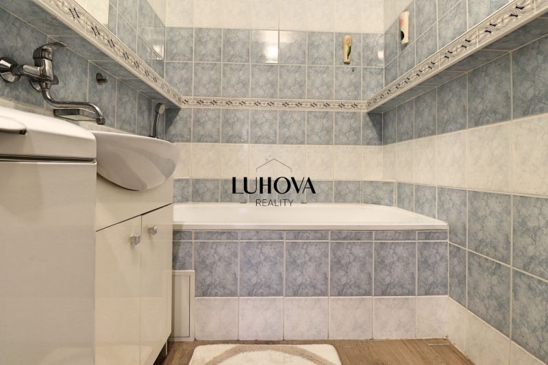 A bathroom in a 3-room apartment with a bathtub and a floor with a wooden decor.