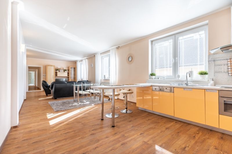A kitchen in a 3-room apartment with a wooden decor floor, seating, bright lighting.