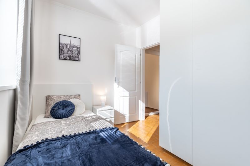 A bright room in a 3-bedroom apartment with a bed and a wooden decor floor.
