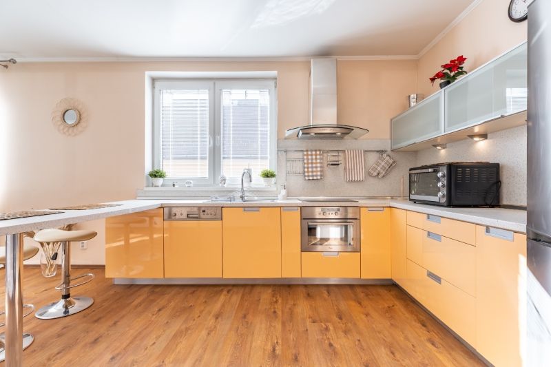 A bright kitchen with orange cabinets and a wood-patterned floor in a three-room apartment.