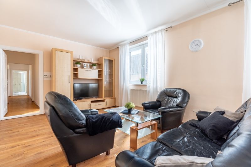 Living room in a three-room apartment with a black leather sofa and a wooden decor floor.