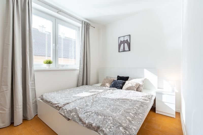 Bright bedroom with wood-patterned flooring in a 3-room apartment, light curtains, nightstand.