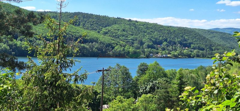 A view of the lake and surrounding hills from the cabin in Bukovec, surrounded by dense forest.