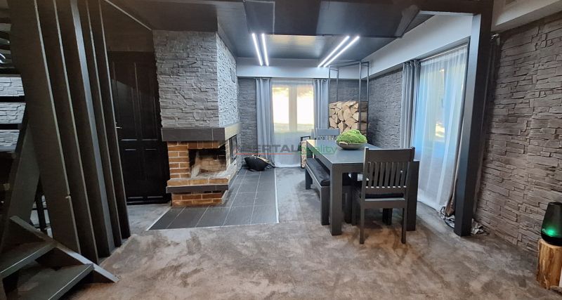 Living area in a cabin with stone cladding and a fireplace, complemented by a dining table.