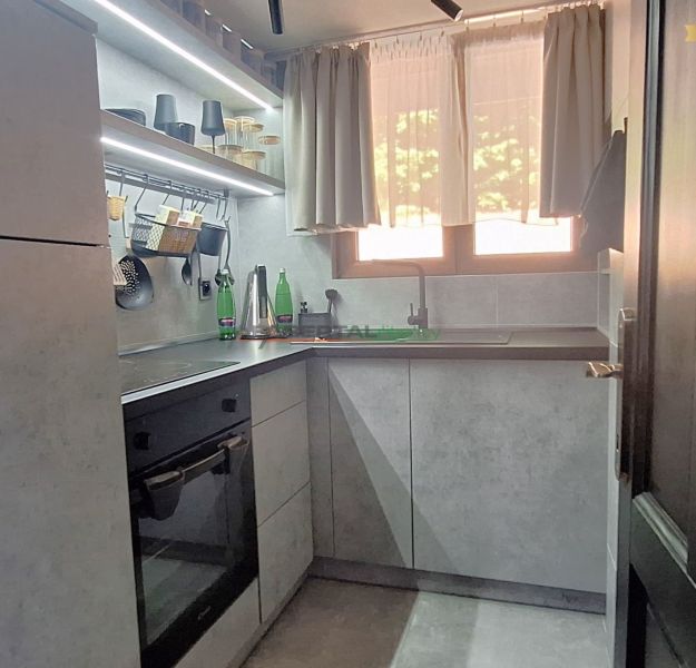 A kitchen in a cottage with a kitchen unit, shelves, and curtains.