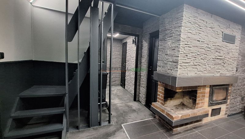 The interior of a cabin with a brick fireplace, staircase, and walls with stone cladding.