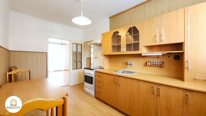 A kitchen in a 2-room apartment with light furniture and a wooden decor floor.