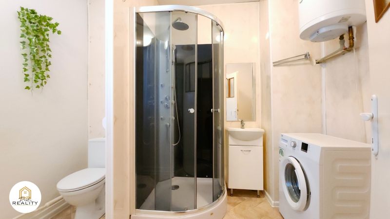 A bathroom in a 2-room apartment with a washing machine, shower, and sink.